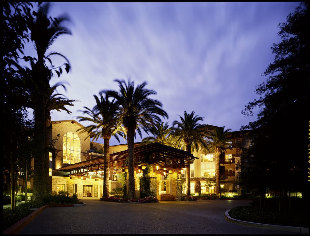 A beautifully lit hotel surrounded by palm trees at dusk.