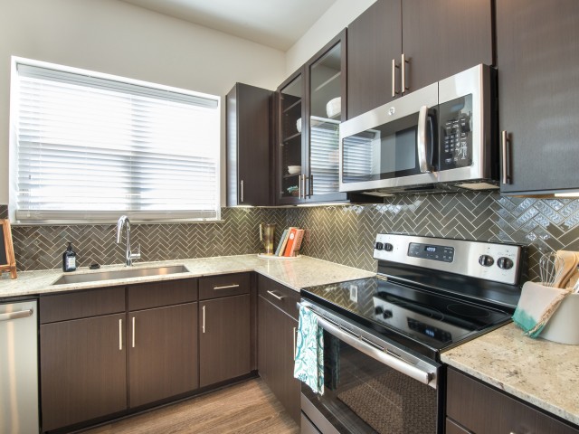 A modern kitchen with dark cabinets and stainless steel appliances.