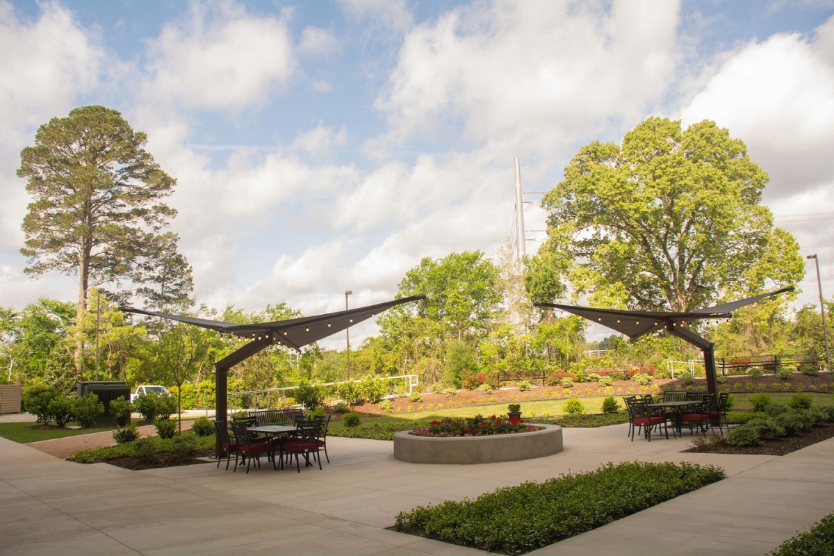 A serene outdoor patio with seating areas under curved structures, surrounded by lush greenery and trees.