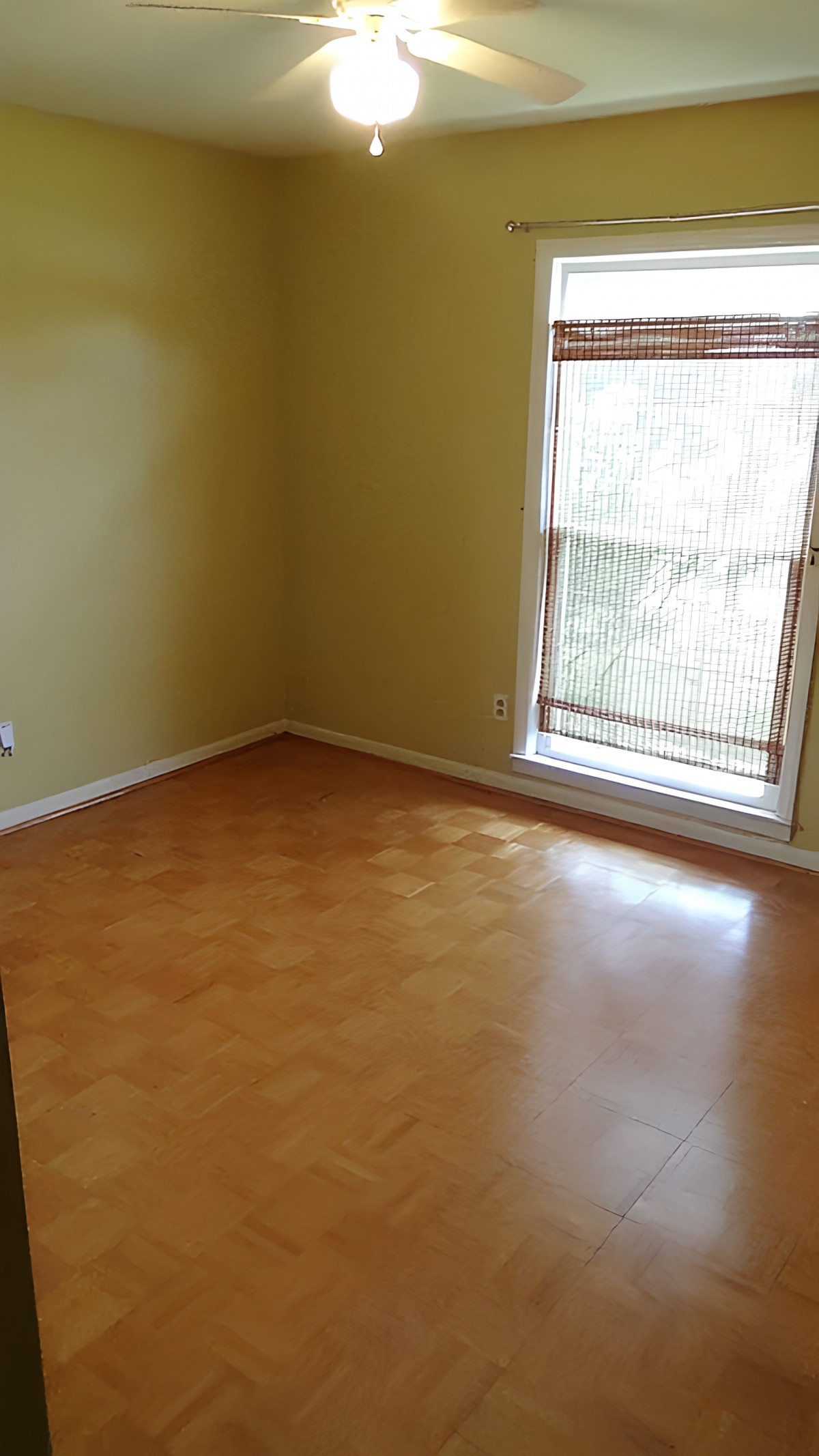 An empty room with yellow walls and a hardwood floor, featuring a window letting in natural sunlight.