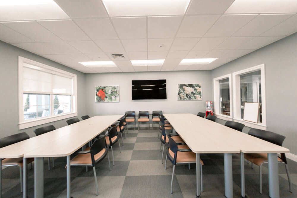 A modern conference room with long tables, multiple chairs, and a television on the wall.