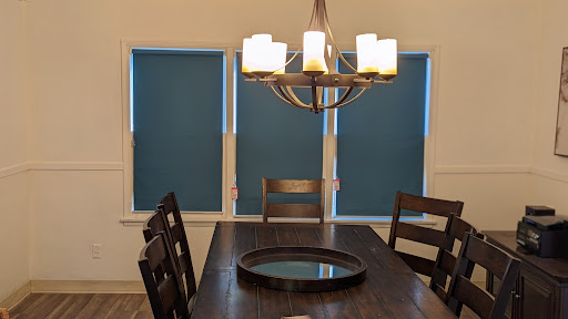 A cozy dining room featuring a wooden table, stylish chairs, and elegant chandelier against blue window shades.
