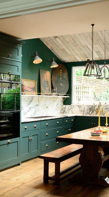 A stylish kitchen with dark green cabinets, a marble backsplash, and modern lighting fixtures.