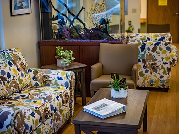 A cozy living room featuring floral-patterned chairs, a coffee table with books and plants, and an aquarium.