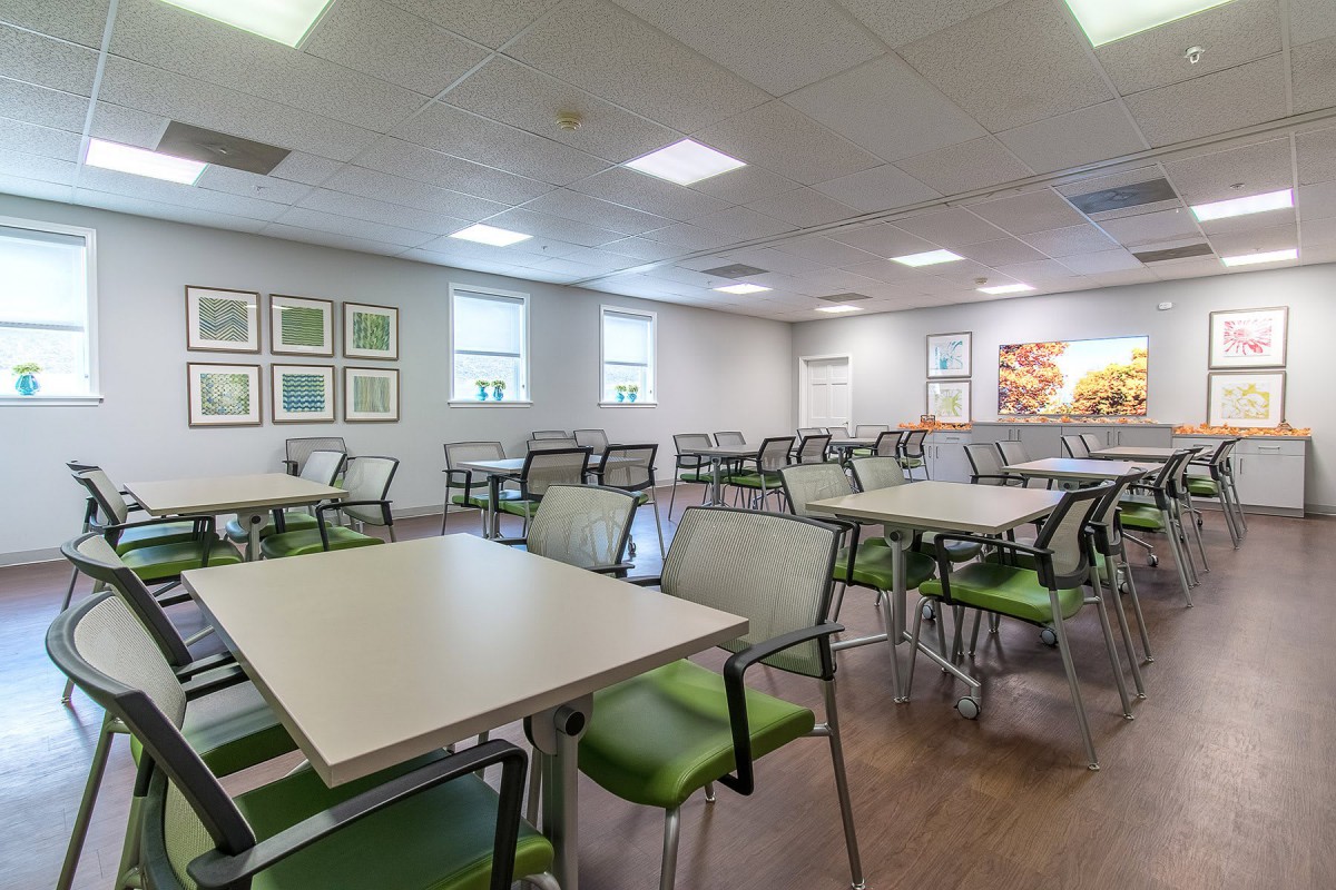 An empty cafeteria with neatly arranged tables and chairs, illuminated by overhead lighting.