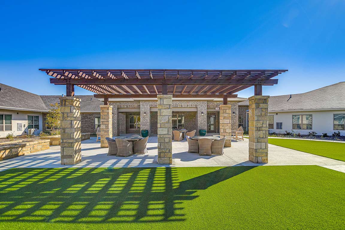 A sunny outdoor patio with a pergola and comfortable seating on a well-maintained lawn.