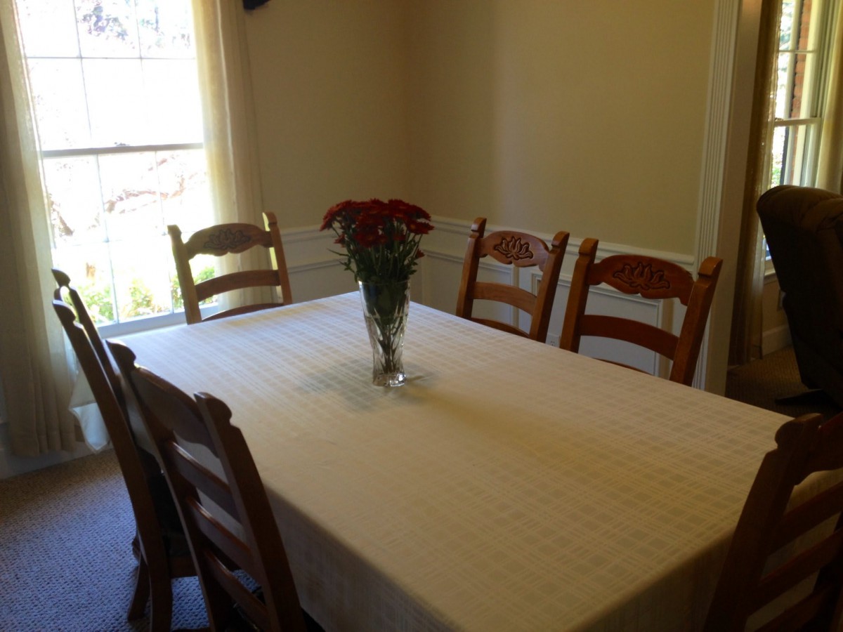 A dining room with a table set for six, featuring a vase with flowers in the center.