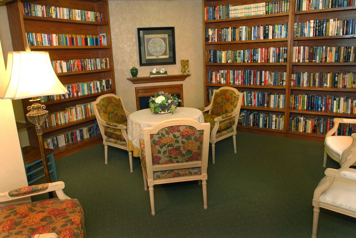 A cozy reading room with bookshelves lining the walls, a round table, and comfortable chairs.
