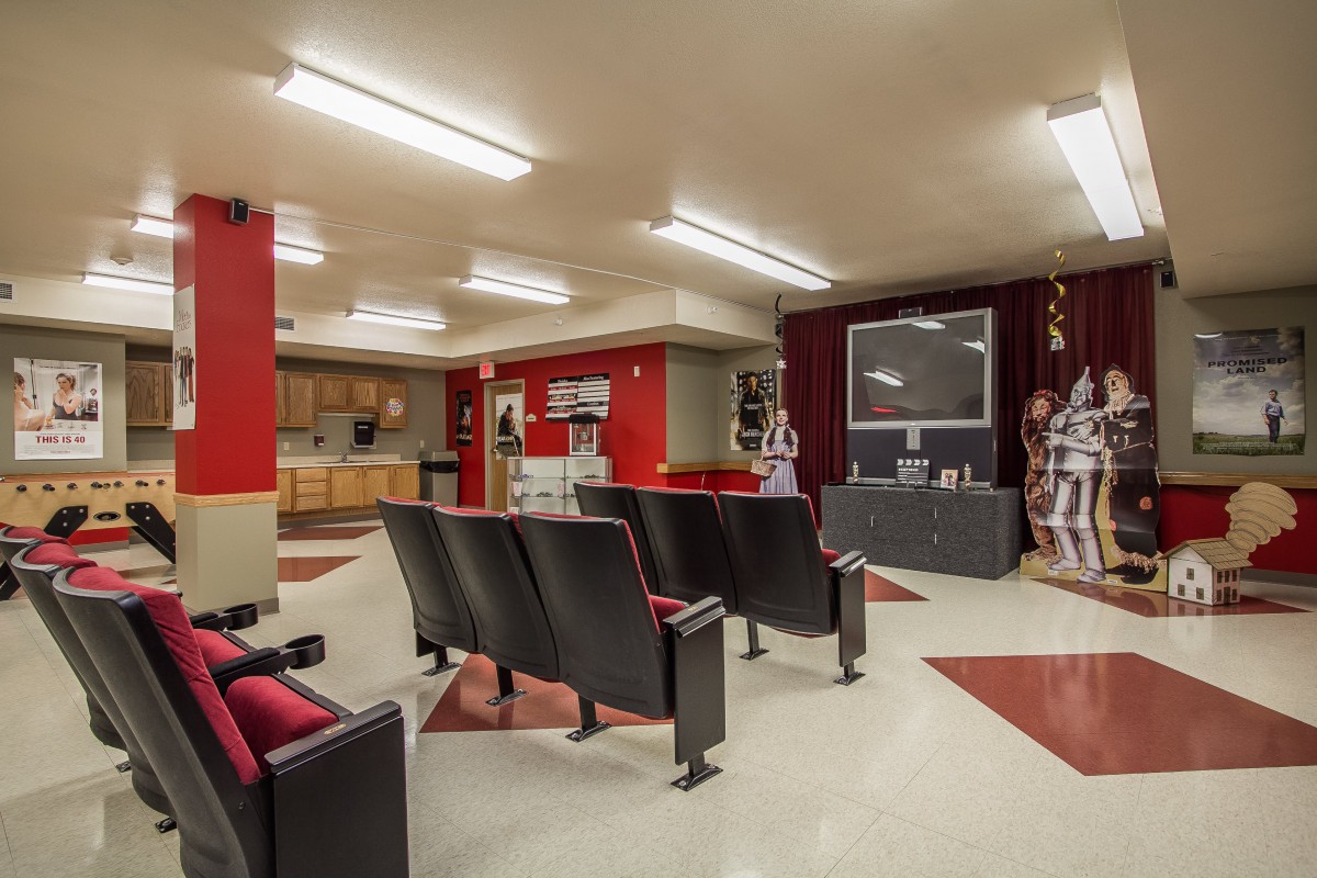 A cozy home theater with a row of cushioned seats facing a large television screen, accented by red and beige decor.