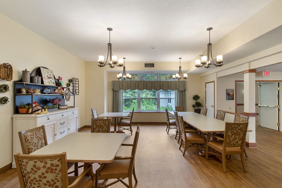 A well-lit dining room with several tables, chairs, and decorative chandeliers.