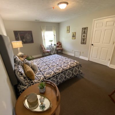 A cozy bedroom featuring a patterned bedspread, a lamp, and decorative art pieces.