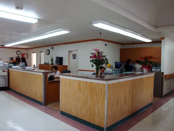 A reception desk in an office setting with flowers and people seated in the waiting area.