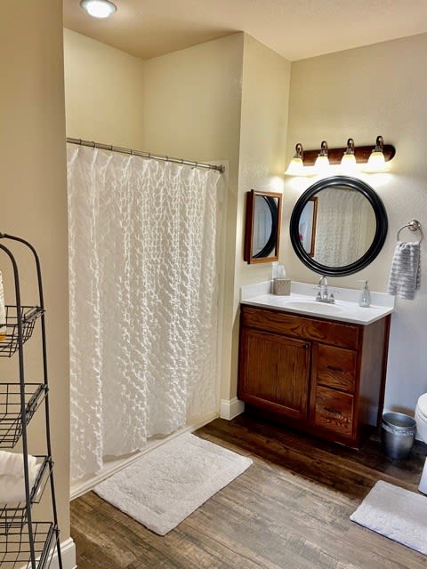 A cozy bathroom with a shower curtain, wooden vanity, and round mirror.