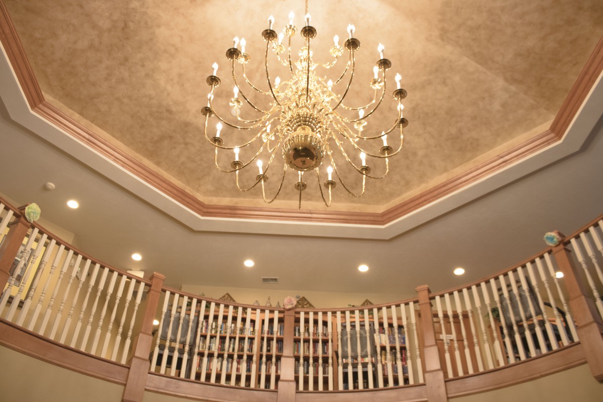 A luxurious chandelier hanging from an ornate ceiling above a curved balcony.