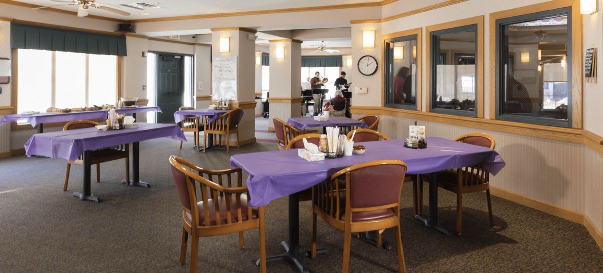 An empty restaurant dining area with tables covered in purple tablecloths.