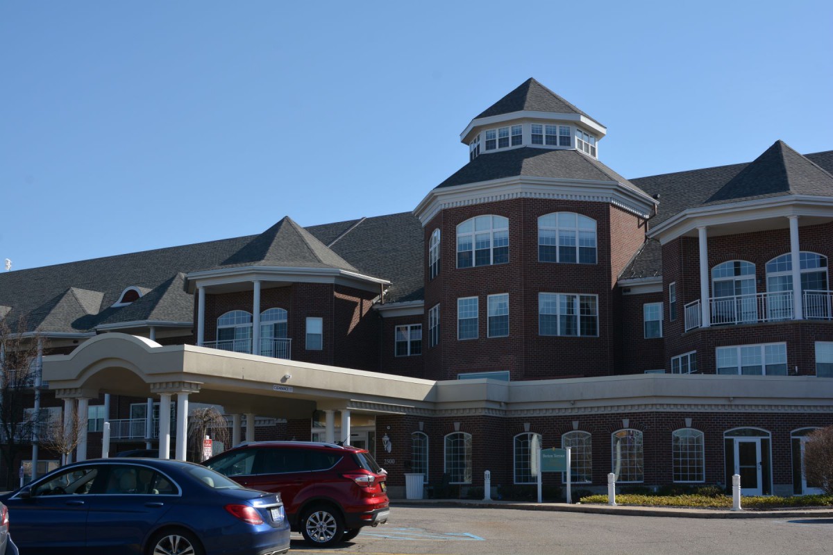 A large, multi-story brick building with a distinctive roof and parked cars in front.