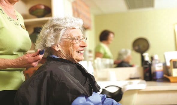 An elderly woman smiling while getting a haircut at a salon.