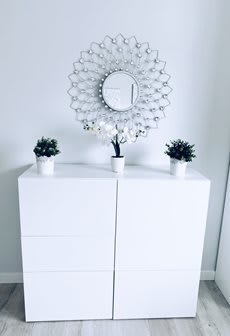 A minimalist white dresser adorned with small potted plants and a decorative mirror.