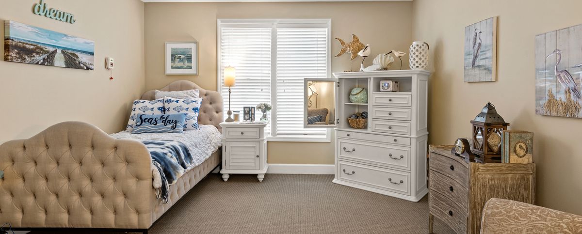 A cozy bedroom with classic white furniture, featuring a bed, nightstand, dresser, and decorative items.