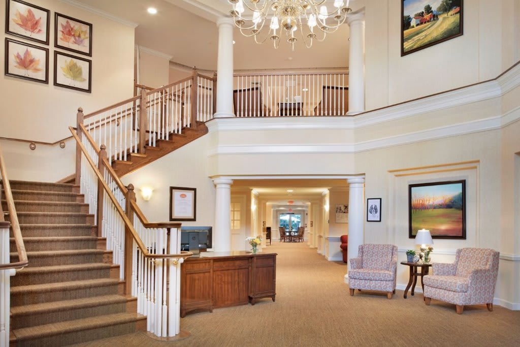 A spacious and elegant lobby with a grand staircase, chandelier, reception desk, and comfortable seating.