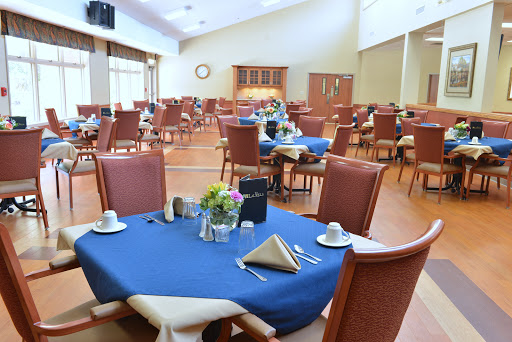 A spacious dining area with neatly arranged tables and chairs, featuring blue tablecloths, ready for guests.