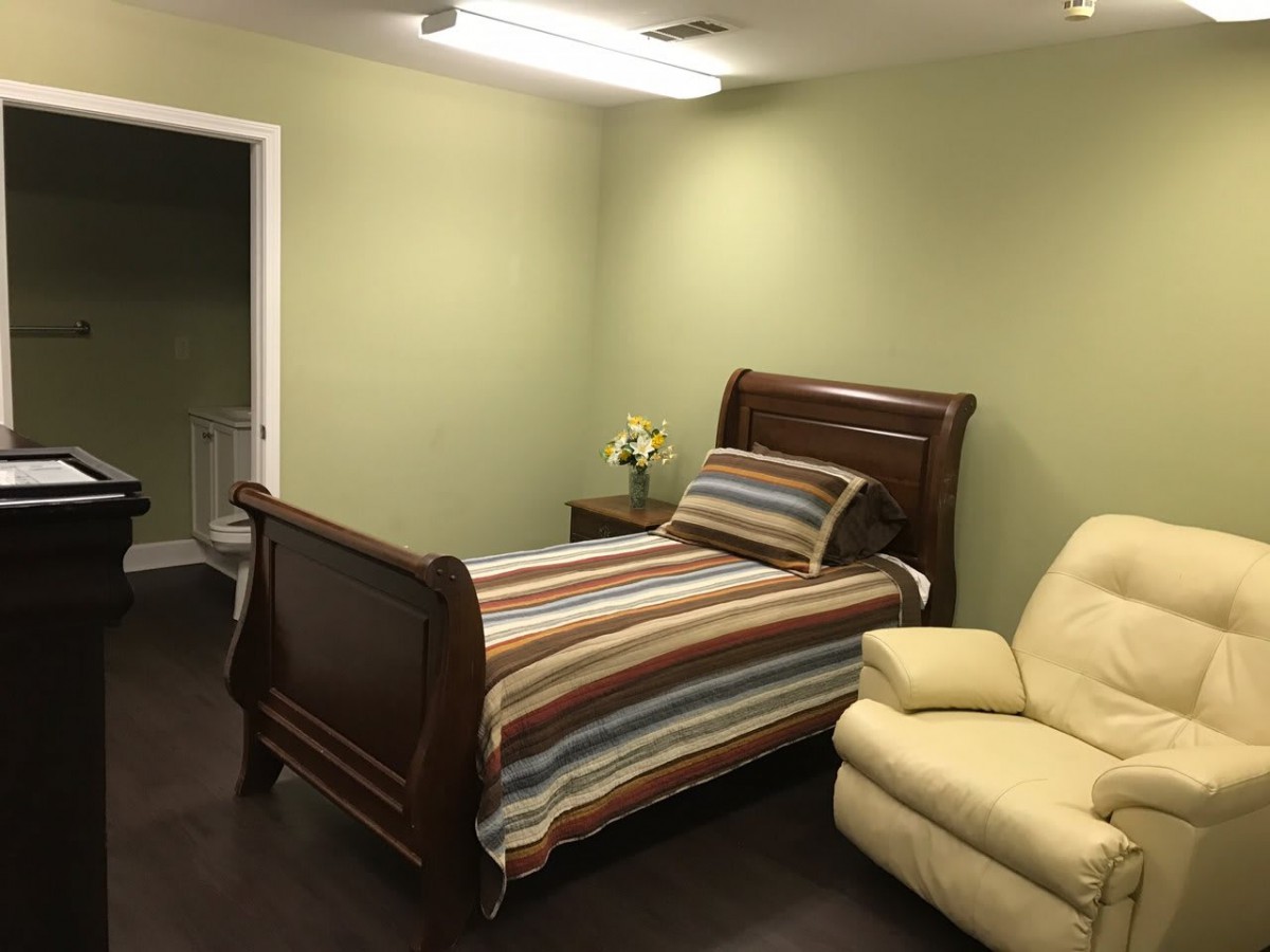 A cozy bedroom with a wooden single bed featuring striped bedding, a recliner chair, and wooden flooring.