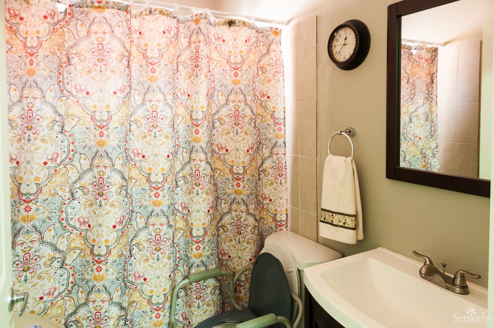A bathroom with a colorful shower curtain, a wall clock, and a sink with a towel.