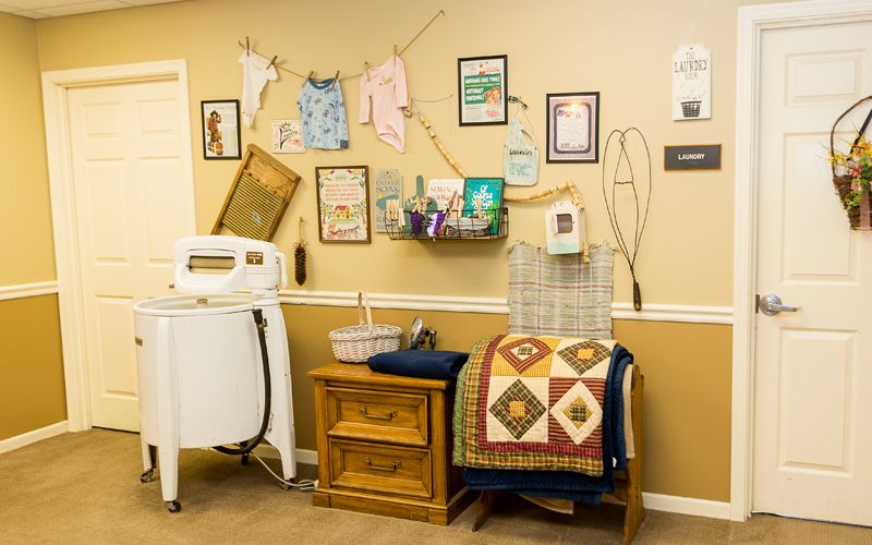 A cozy laundry room with vintage decor, including a quilt and wall art.