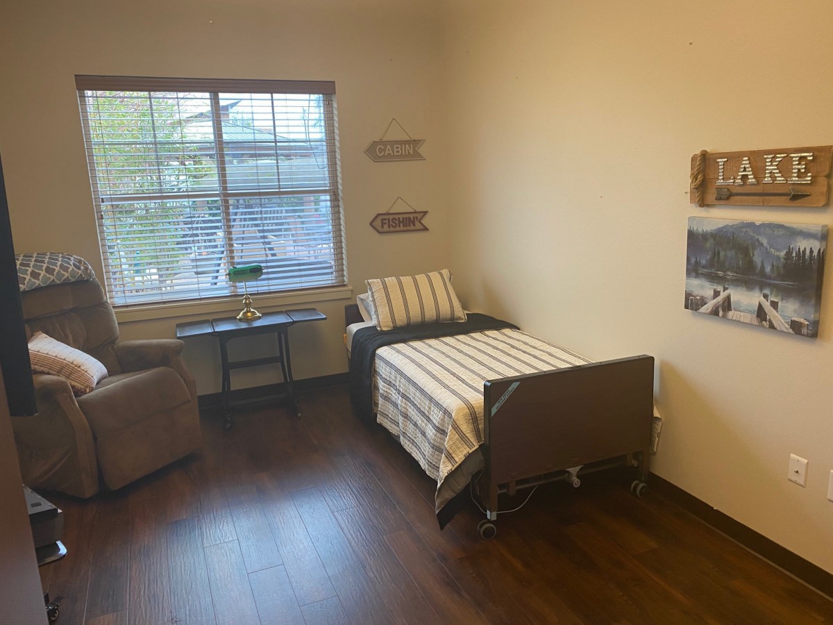 A minimalist room with a hospital bed, armchair, and window providing natural light.