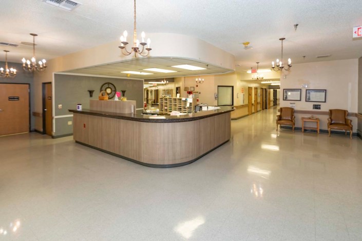 An empty hospital reception area with a central desk and a bright, well-lit hallway.