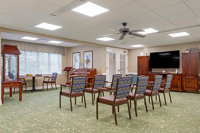 A well-arranged meeting room with rows of chairs, a television, and a ceiling fan.
