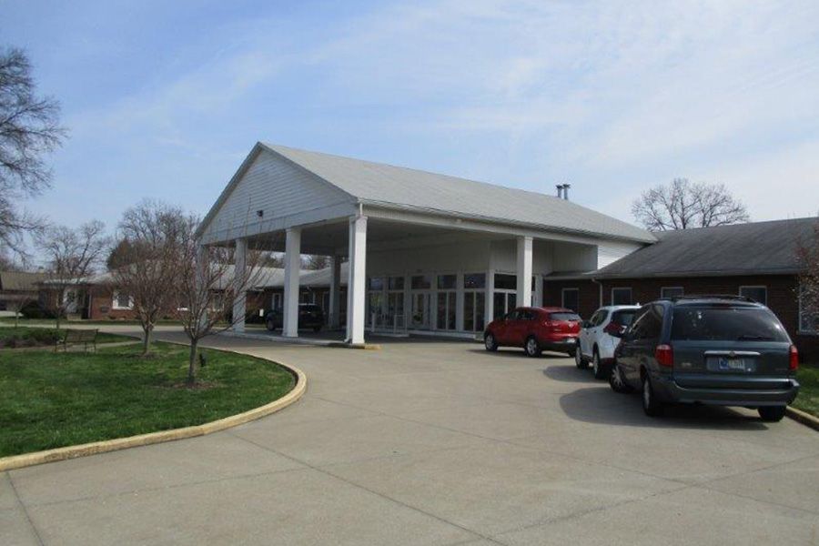 A building with a covered entrance, featuring several parked cars in the driveway.