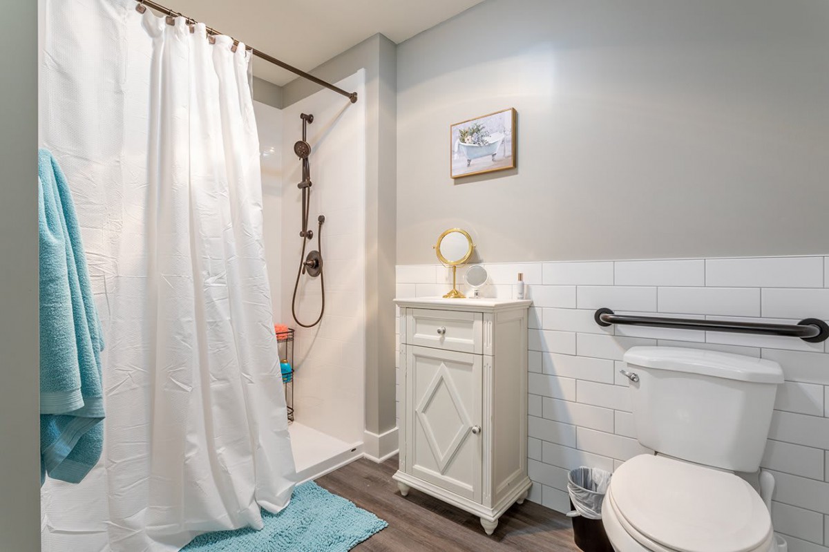 A modern bathroom featuring a shower with a white curtain, a small vanity with a mirror, and a toilet.