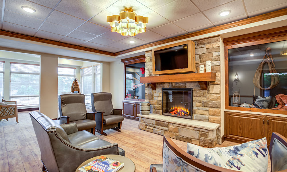 A cozy living room with a stone fireplace, comfortable chairs, and a television mounted above the mantel.