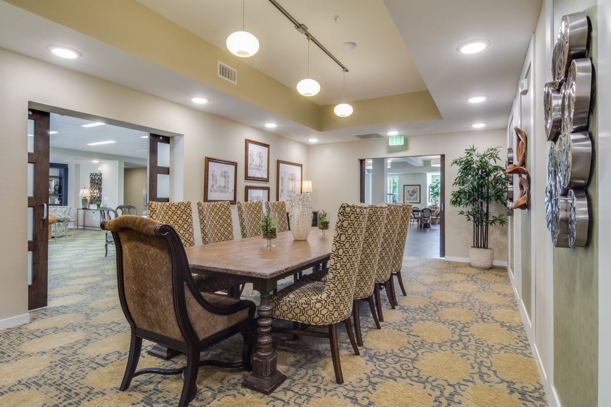 A spacious and elegantly decorated dining room with a large table and upholstered chairs, featuring modern lighting and artwork.