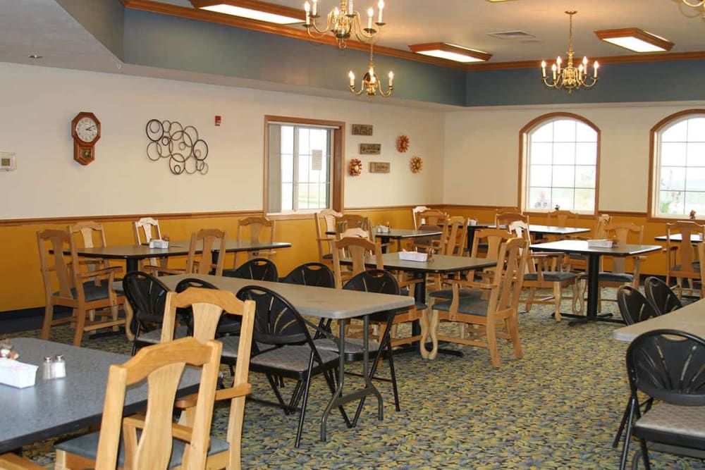 An empty dining area with neatly arranged tables and chairs, accented by chandeliers and wall decorations.