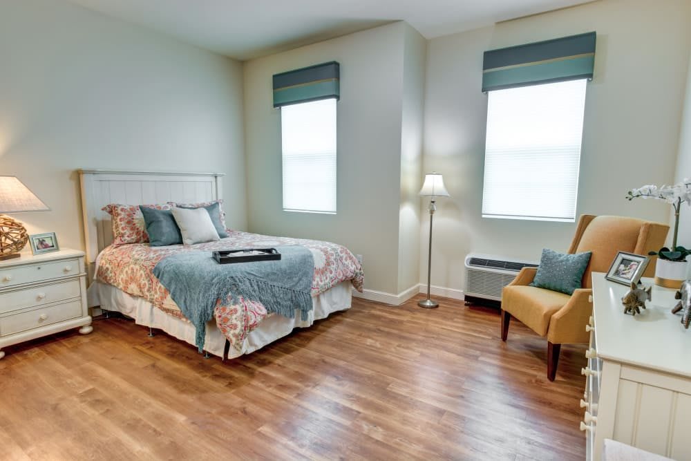 A cozy bedroom with a neatly made bed, a floor lamp, and a comfortable chair.