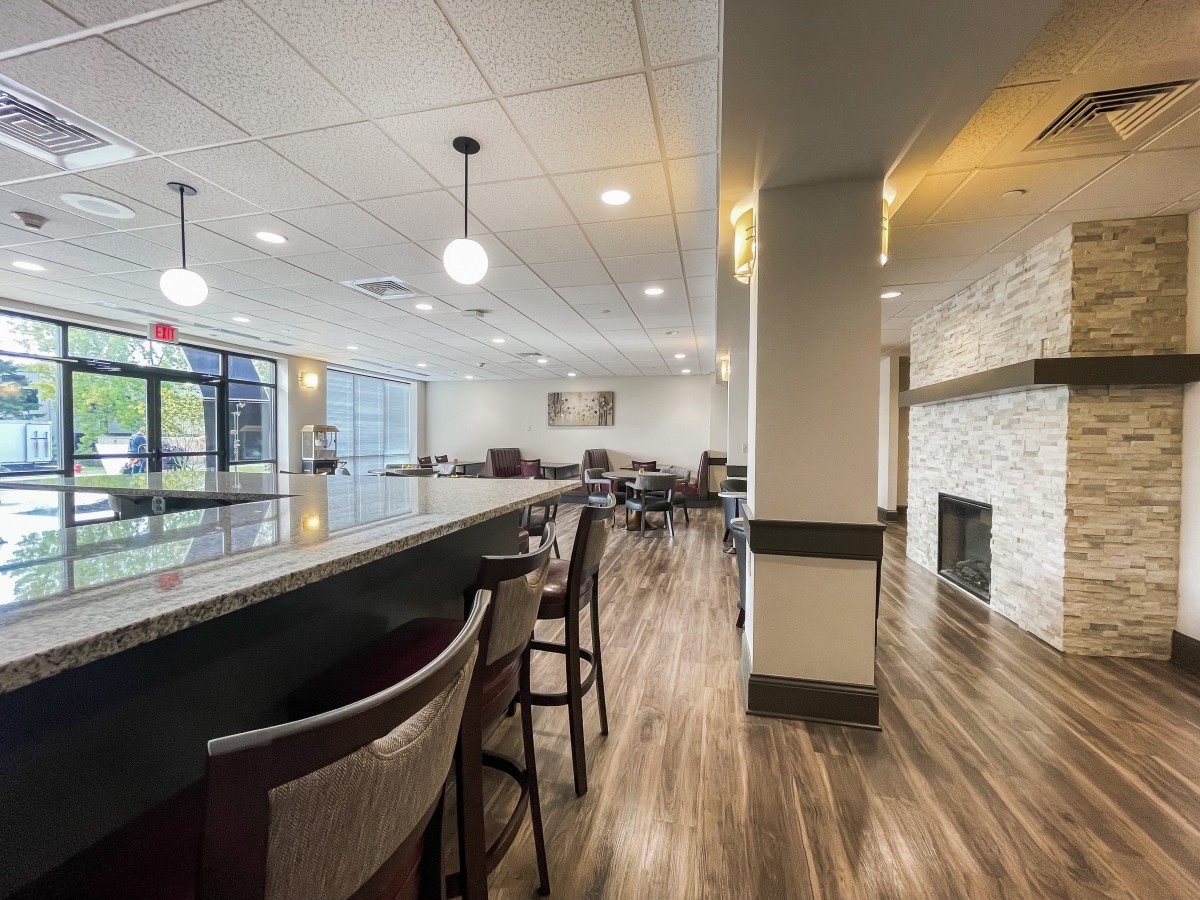 A modern restaurant interior with a bar area, featuring wood flooring and contemporary lighting.