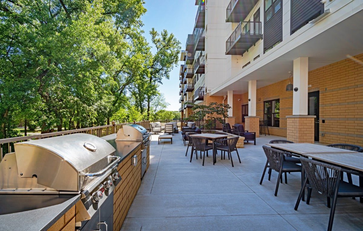 A spacious outdoor patio with grills and seating next to an apartment building.