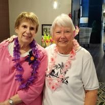 Two women smiling indoors, wearing lei necklaces.