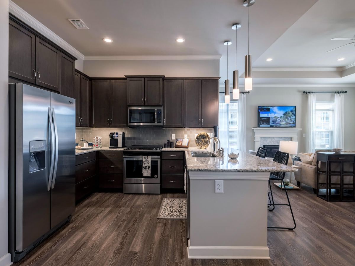 A modern kitchen with dark cabinets, stainless steel appliances, and pendant lighting opens into a cozy living area.