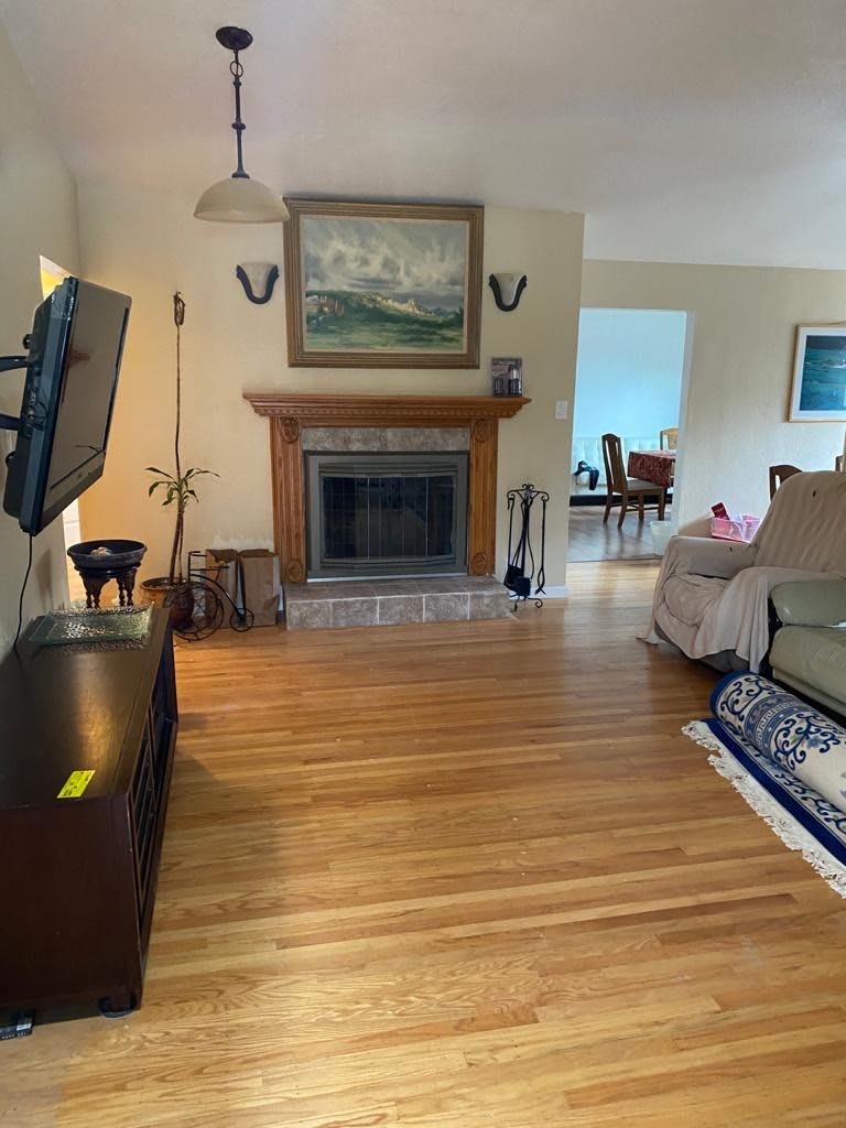 A cozy living room with a hardwood floor, featuring a fireplace and a painting above it.