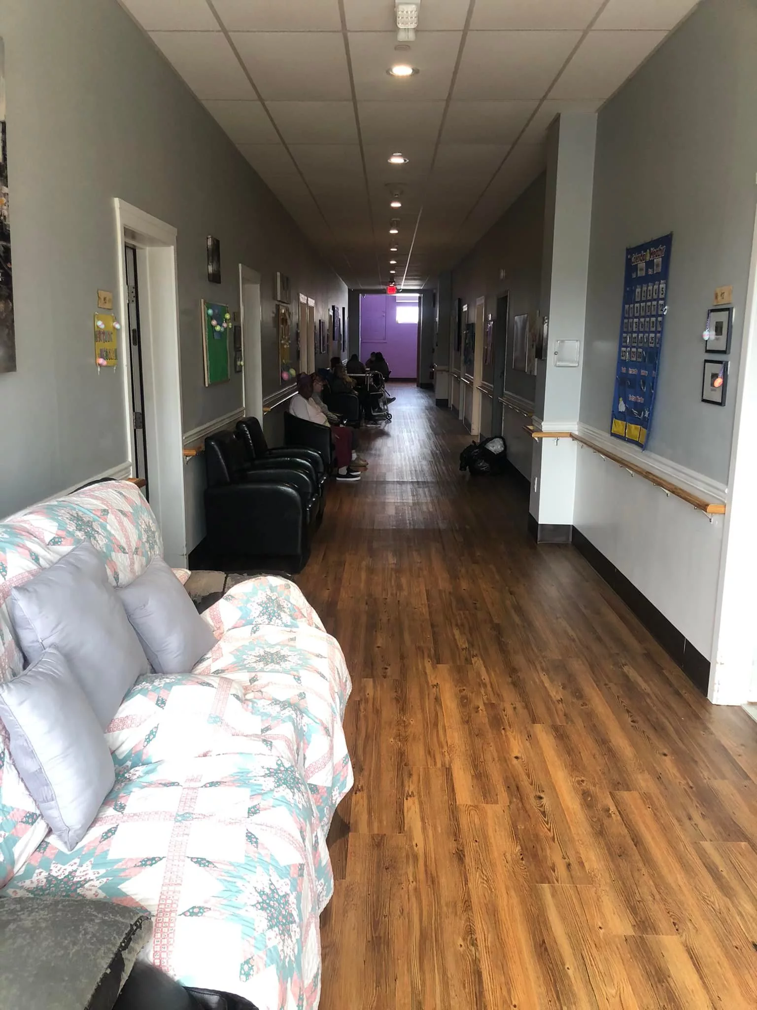 A long hallway with wooden flooring, featuring a floral sofa and chairs along the sides.