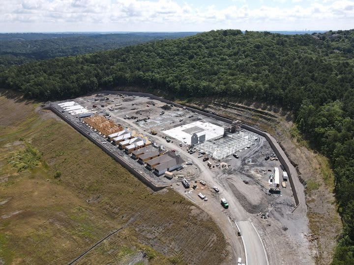 Aerial view of a construction site amidst a wooded area, showcasing ongoing building and land development.
