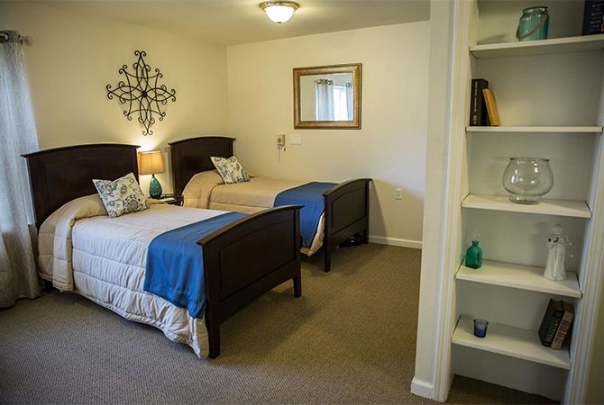 A cozy bedroom featuring twin beds with blue throws, a decorative wall piece, and built-in shelving.