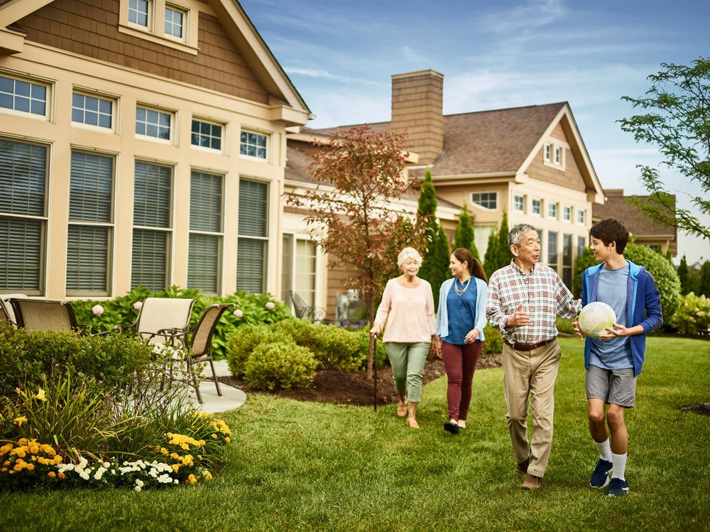 A family walking together in a garden outside a large house.