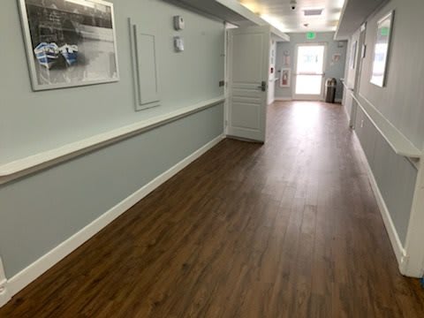 A long hallway with wooden flooring and picture frames on the wall.