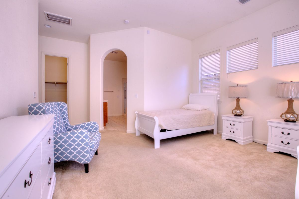 A cozy bedroom with a single bed, patterned armchair, and elegant lamp.