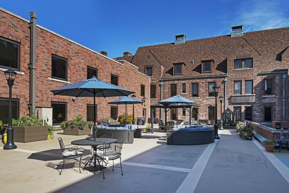 A tranquil courtyard with outdoor seating and umbrellas set against a charming brick building.