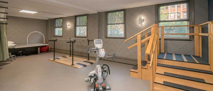 A well-equipped indoor gym with an exercise bike, parallel bars, and a staircase for rehabilitation exercises.